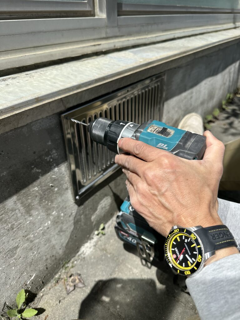 床下換気口にカバーをつけているスタッフ